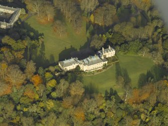 Oblique aerial view centred on the house with the stable block adjacent, taken from the S.