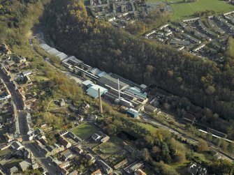 Oblique aerial view centred on the mill and chimney stack, taken from the NW.