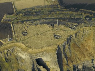 Oblique aerial view centred on the remains of the battery with Macduff's cave in the foreground, taken from the SSE.