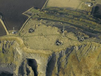 Oblique aerial view centred on the remains of the battery with Macduff's cave in the foreground, taken from the ESE.