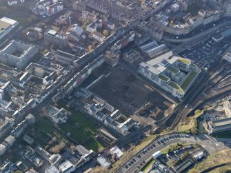 Oblique aerial view centred on the cleared Caltongate development site (former SMT bus garage) with Canongate adjacent, taken from the NE.