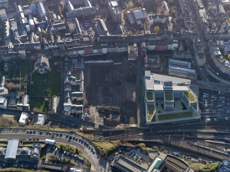 Oblique aerial view centred on the cleared Caltongate development site (former SMT bus garage) with Canongate adjacent, taken from the NNW.