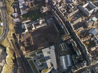 Oblique aerial view centred on the cleared Caltongate development site (former SMT bus garage) with Canongate adjacent, taken from the W.