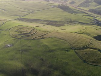 Oblique aerial view centred on the remains of the fort and linear earthwork with the remains of the linear earthwork and pit-alignment adjacent, taken from the NE.