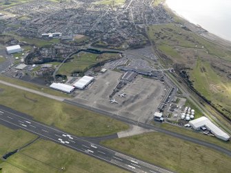 Oblique aerial view centred on the airport terminal buildings with the railway station adjacent, taken from the N.