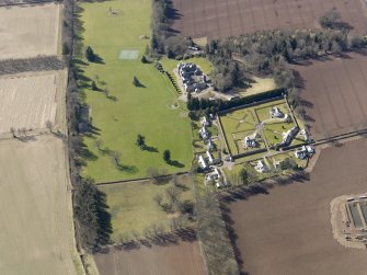 Oblique aerial view centred on the country house, its policies and the modern housing development, taken from the NE.