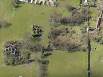 Oblique aerial view centred on the remains of the house with the remains of the stables adjacent, taken from the E.
