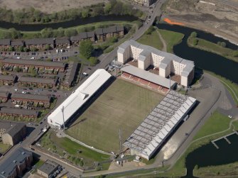 Oblique aerial view centred on the football ground with the apartment block adjacent, taken from the SE.