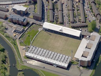 Oblique aerial view centred on the football ground with the apartment block adjacent, taken from the NE.