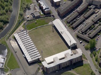 Oblique aerial view centred on the football ground with the apartment block adjacent, taken from the N.