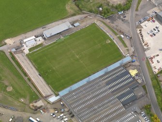 Oblique aerial view centred on the football ground with the auction mart adjacent, taken from the SW.