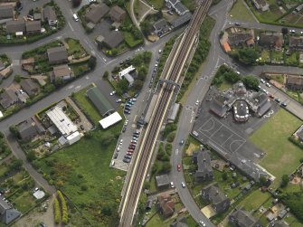 Oblique aerial view centred on the railway station with the school adjacent, taken from the SSE.