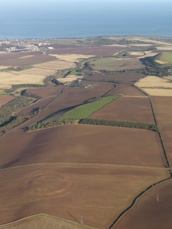 General oblique aerial view of the soilmarks of the fort of The Chesters, Spott, with the coast in the distance, taken from the SW.