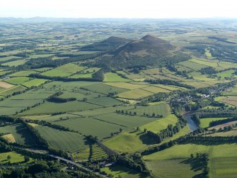 General oblique aerial view looking across the bridge, viaduct, village and site of the Roman fort  towards the fort and Eildon Hills, taken from the NNE.