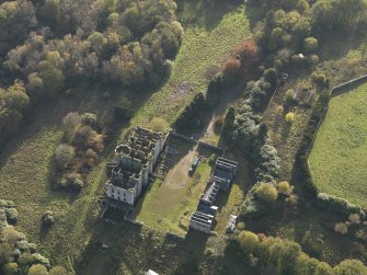 Oblique aerial view centred on the ruins of the country house with the stables adjacent, taken from the NNE.
