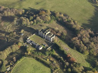 Oblique aerial view centred on the ruins of the country house with the stables adjacent, taken from the W.