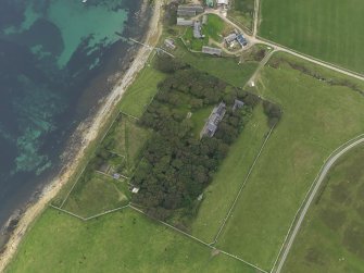 Oblique aerial view centred on the house with the remains of the chambered mound adjacaent, taken from the SSE.