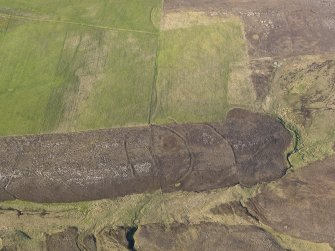 Oblique aerial view centred on the remains of the round house, enclosures, banks and a trackway on Peerie Hill, taken from the SSW.