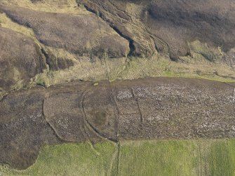 Oblique aerial view centred on the remains of the round house, enclosures, field banks and a trackway on Peerie Hill, taken from the NNE.