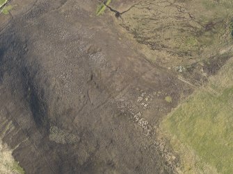 Oblique aerial view centred on the remains of the round house, enclosure and field banks on the summit of Billia Fiold, taken from the NW.