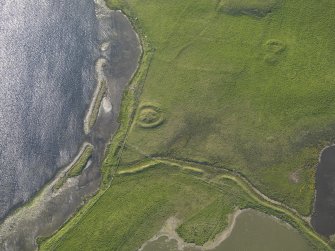 Oblique aerial view centred on the barrow at Bookan with the remains of the cairns and field boundaries adjacent, taken from the SE.