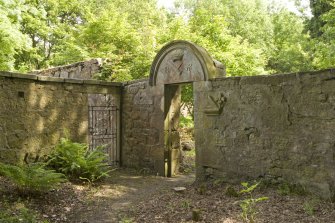 View of main gateway to Robertland walled garden, with round arched pediment and carved stone fragments set into the wall, salvaged from old Robertland Castle.