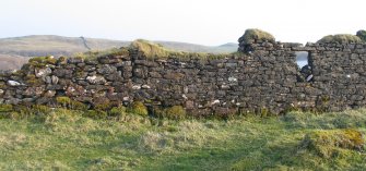 External view of north west wall of south-west houses. Shows the superior stone work of the right house and the rebuilding of the wall of the left house from about half way up;  large stones in foundations which overlap the joint wall of the two houses; blocked window to right of centre and remaining window.