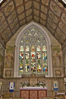 Interior. E wall of chancel and stained glass window, view from W