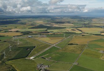 General oblique aerial view centred on the remains of the airfield with the windfarm adjacent, taken from the ENE.