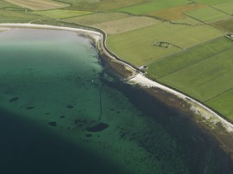 Oblique aerial view centered on the pier at Evie with St Nicholas' Chapel adjacent, taken from the N.