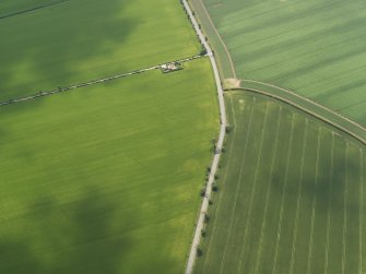 Oblique aerial view centred on the cropmarks of the round house and pits, taken from the NNE.