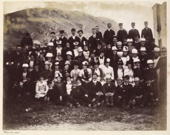 View of large group of people including a number of men and boys in railway uniforms and ladies with fancy hats, possibly in Lendalfoot.


