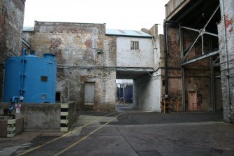 View. West Yard (Central): view looking north, under Building 10 (former Rag Store) towards Effluent Treatment Plant (Building area 5).Southern Railway Access on left, behind blue Sodium Hypo silo.