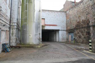 View. West Yard (Central) (area 9), looking south, under building rear of Building 13 with Starch Silo at centre left.