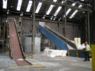 Interior. Building 1, Wood Pulp Store, conveyors 1and 2 of 3. Pulp visible in pile to left of right hand conveyor. Brian Malaws (RCAHMW in red hat)  and Charles Whittaker (production manager, in orange protective hat).