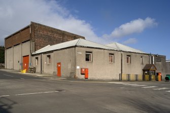 Canteen, 84 Vintner Street (elevation onto Harvey Street), and Stores at 90 Vintner Street, view from SW. The gable end of no. 90 retains some earlier brickwork dating from between 1867 and 1896 (building footprint does not exist before 1867 according to the Ordnance Survey map). Both these buildings are harled thus obscuring the age of the structures. Note the blocked cart entrance to the left of the bright red door.