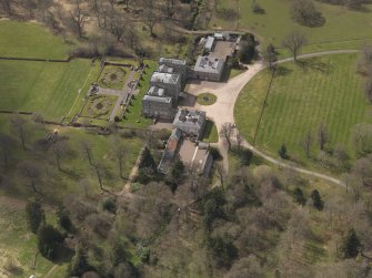 Oblique aerial view centred on the country house with the stable block adjacent, taken from the NE.