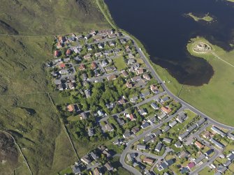 Oblique aerial view of the housing on the W shore of the Loch of Clickhimin with the remains of the broch and settlement of Clickhimin adjacent, looking NE.