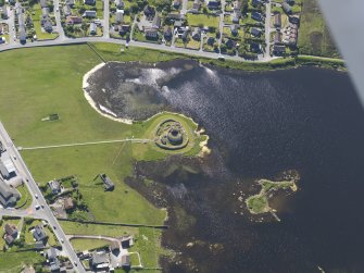 Oblique aerial view centred on the remains of the broch and settlement of Clickhimin, looking W.