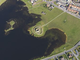 Oblique aerial view centred on the remains of the broch and settlement of Clickhimin, looking SE.