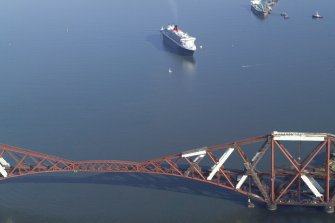 Oblique aerial view of the Queen Mary 2 with the Forth Rail Bridge in the foreground, taken from the WSW.