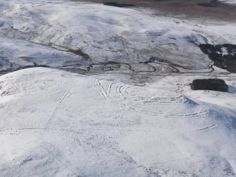 General oblique aerial view of Woden Law fort and linear earthworks in snow, looking WNW.