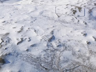 General oblique aerial view of cairn, farmsteads, sheepfold, enclosure and rig and furrow under snow, looking to NW.