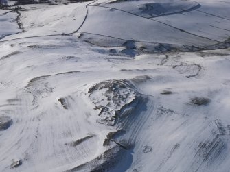 Oblique aerial view of fort, settlement and palisaded enclosure, rig and furrow and field boundaries under snow, looking to W.