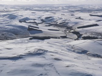 General oblique aerial view of fort, settlement and palisaded enclosure, rig and furrow and field boundaries under snow, looking to SW.