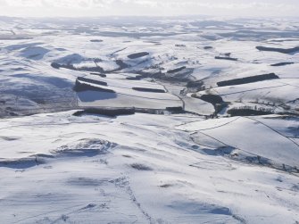 General oblique aerial view of fort, settlement and palisaded enclosure, rig and furrow and field boundaries under snow, looking to SW.