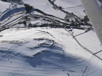 General oblique aerial view of scooped settlement, settlement and cultivation terraces under snow, looking to WSW.