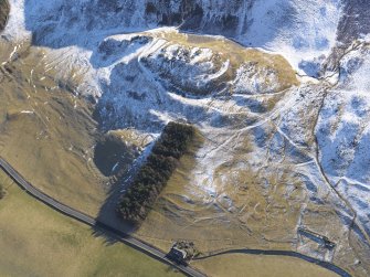 Oblique aerial view of Tinnis Castle and fort, building, platform, settlement and track, enclosure and a burnt mound under snow, looking E.