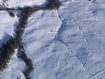 Oblique aerial view of the buildings, small cairns, field boundaries and trackways, looking E.