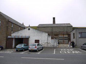 View of the main entrance to the gasworks from John Street showing the retort house behind. The white, single-storey building was the original coal store. To the right of this was the gasworks manager's house.  The replaced roof on the retort house can be seen.